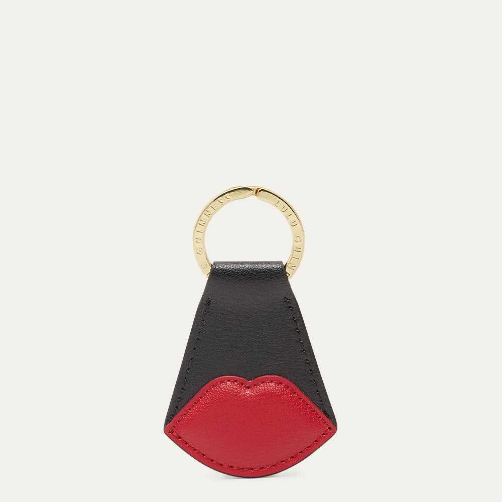 Black and red lip-shaped keychain with a gold ring on a white background