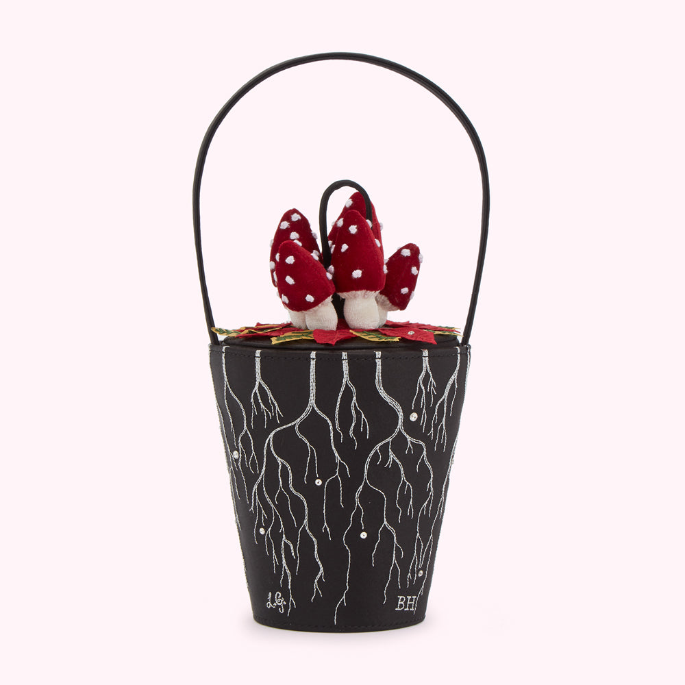 Black satin bucket bag with a handle, adorned with embroidered roots and topped with felt mushrooms.