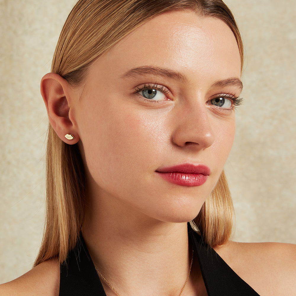 Close-up of a woman's face wearing a lip-shaped gold stud earring with a neutral background