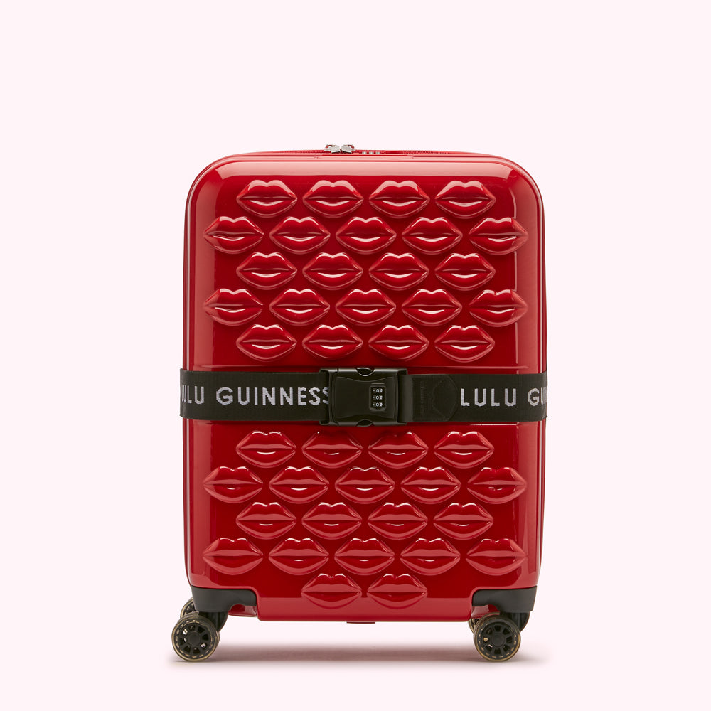 Red Lulu Guinness suitcase with a lip print and a black luggage strap.