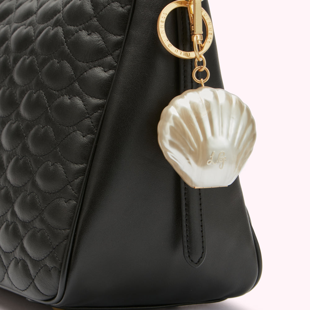 Close-up of a black quilted leather handbag with a pearl-shaped charm attached.