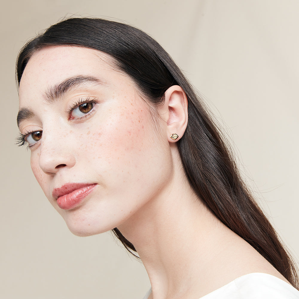 Close-up of a woman wearing a gold lip shaped earring against a neutral background