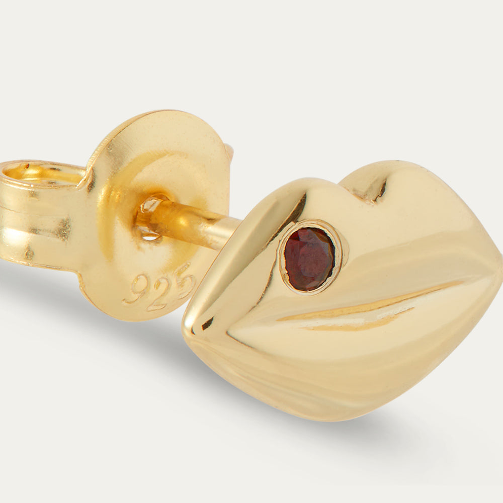 Gold earring with a red gemstone on a light grey background