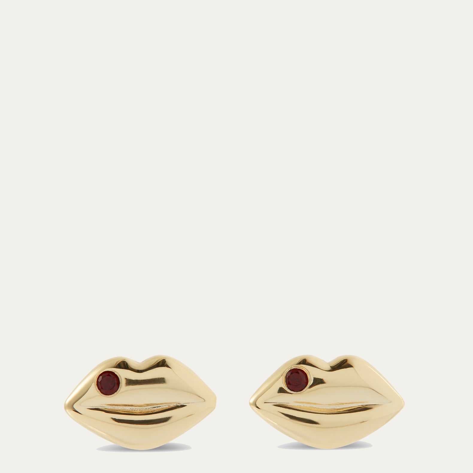 Gold earrings shaped like lips with red gemstones on a white background