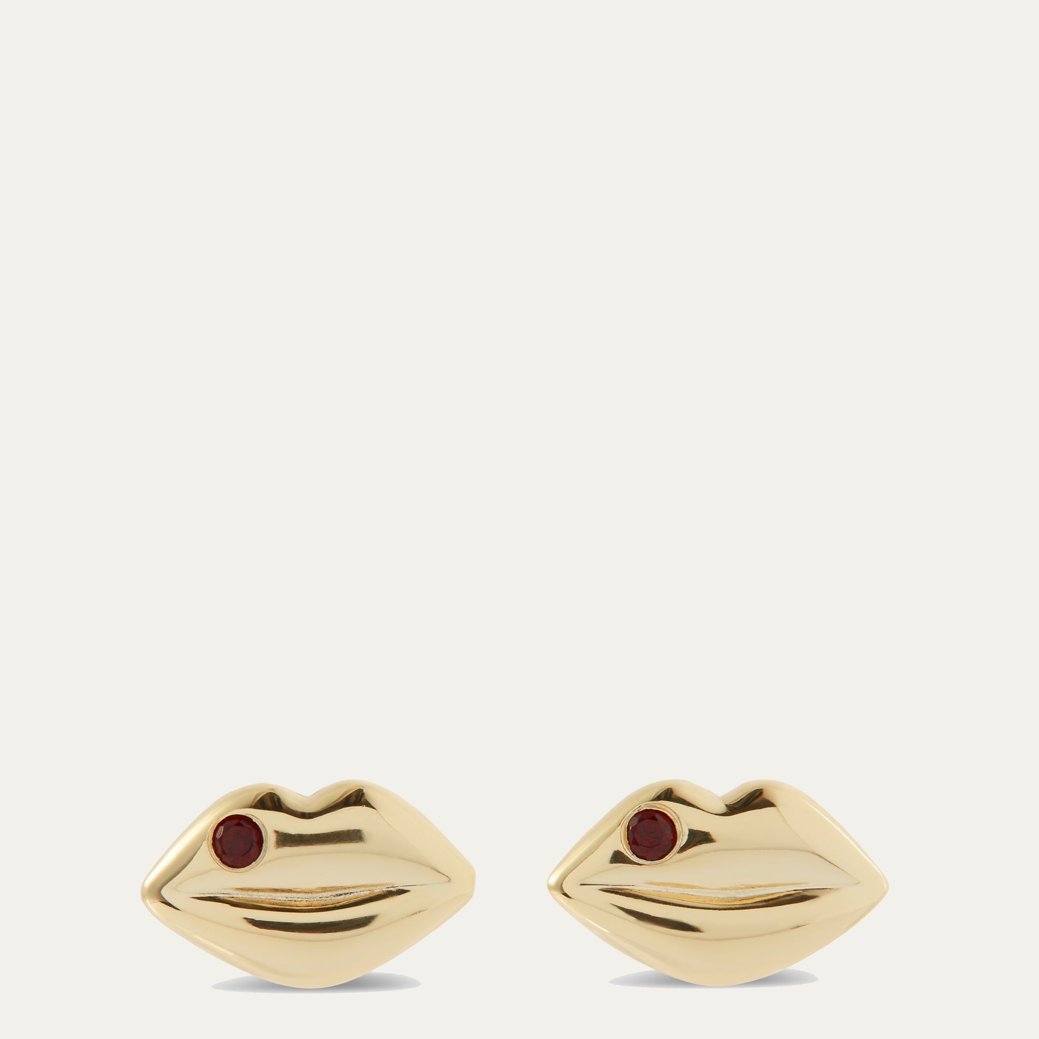 Gold earrings shaped like lips with red gemstones on a white background