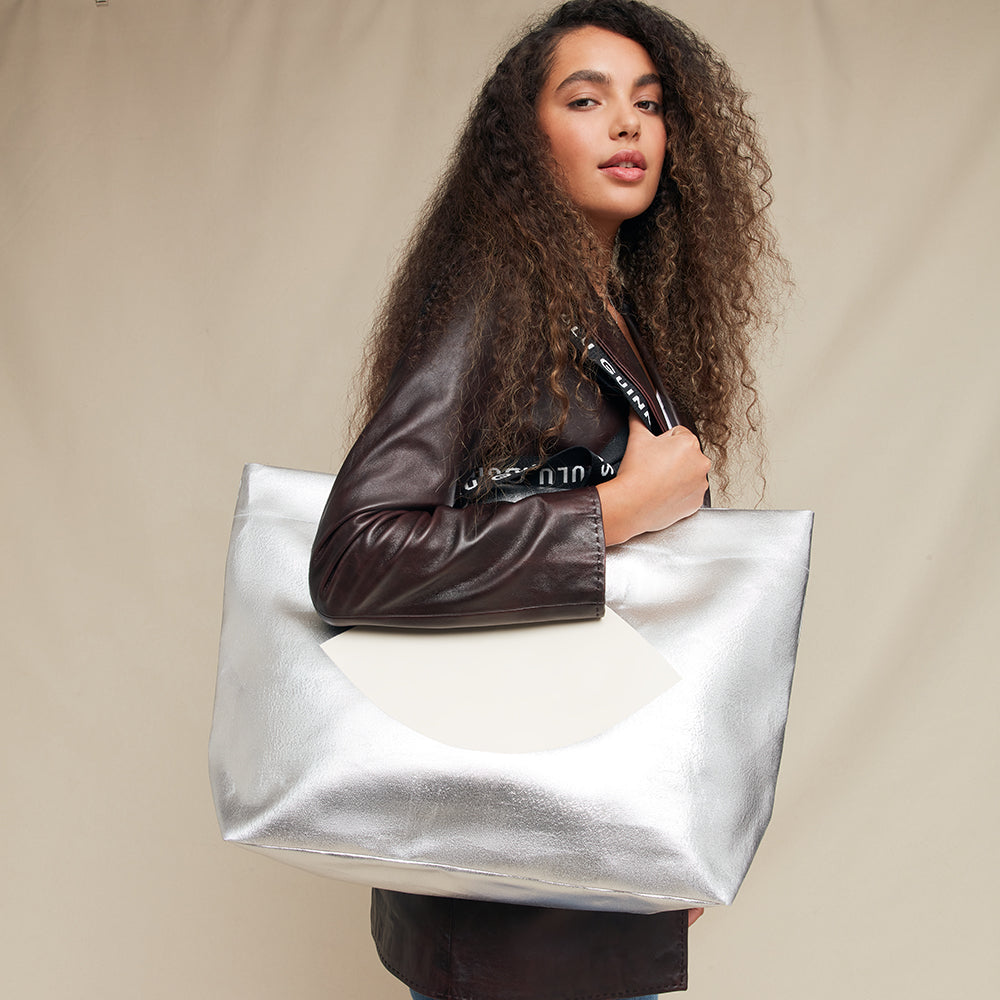 Woman holding a silver metallic handbag against a beige background