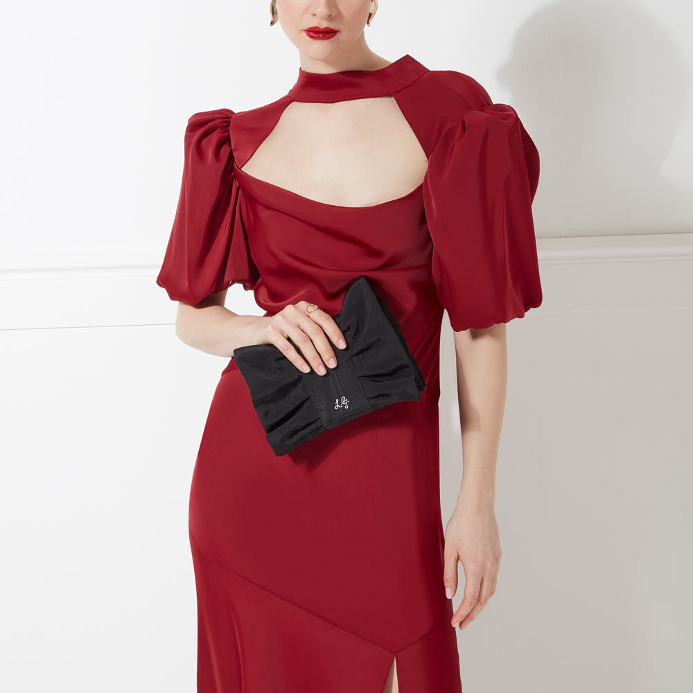Woman in a red dress holding a black bow-shaped clutch.
