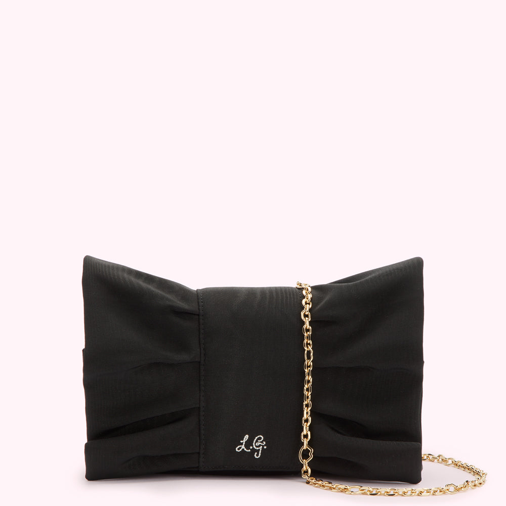 Black bow-shaped clutch with gold chain strap and subtle logo.
