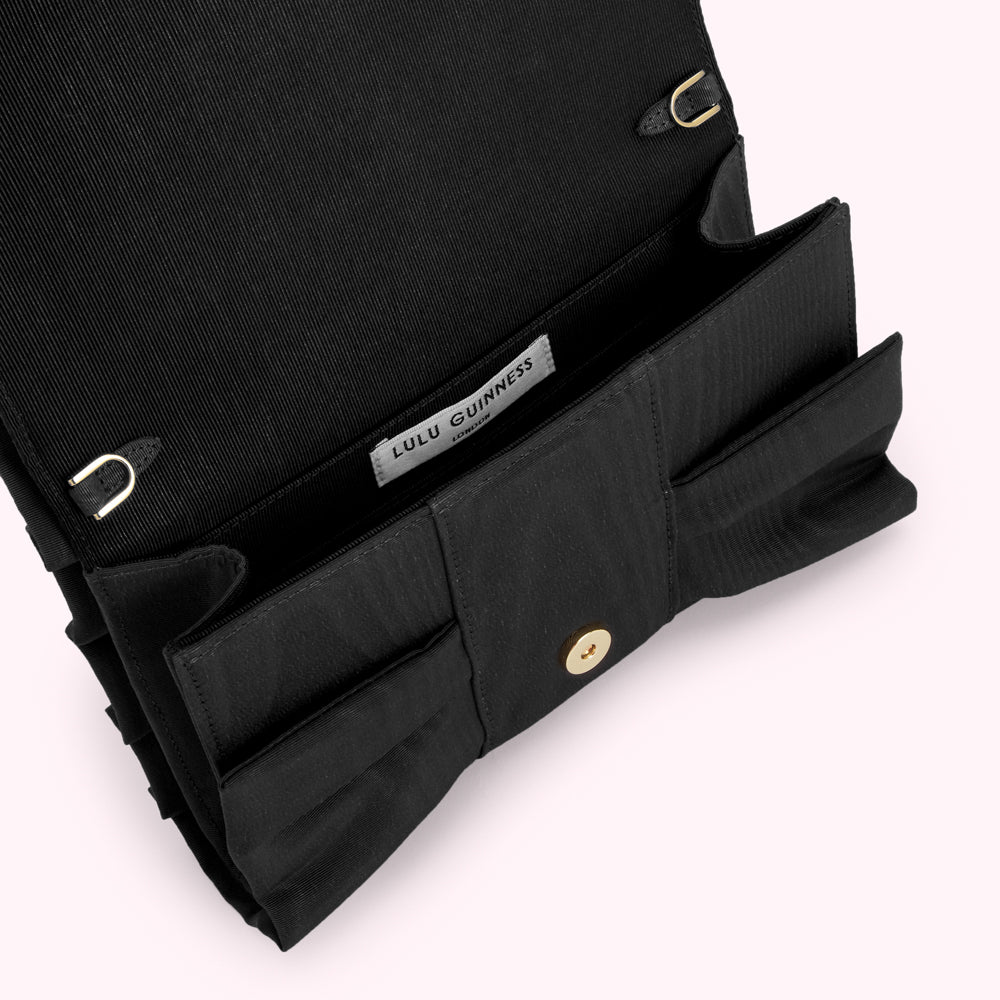 Black Lulu Guinness bow clutch bag open to reveal the interior and brand label.