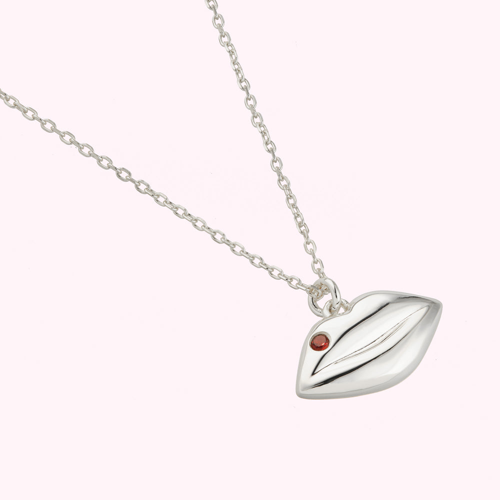 Close up detail of Sterling silver solid lip pendant charm on a chain featuring a inset Ruby precious stone.