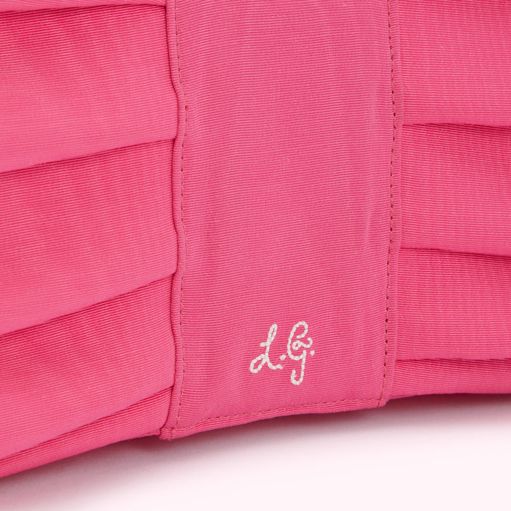 Close-up of a hot pink pleated fabric bag with a subtle embossed logo.
