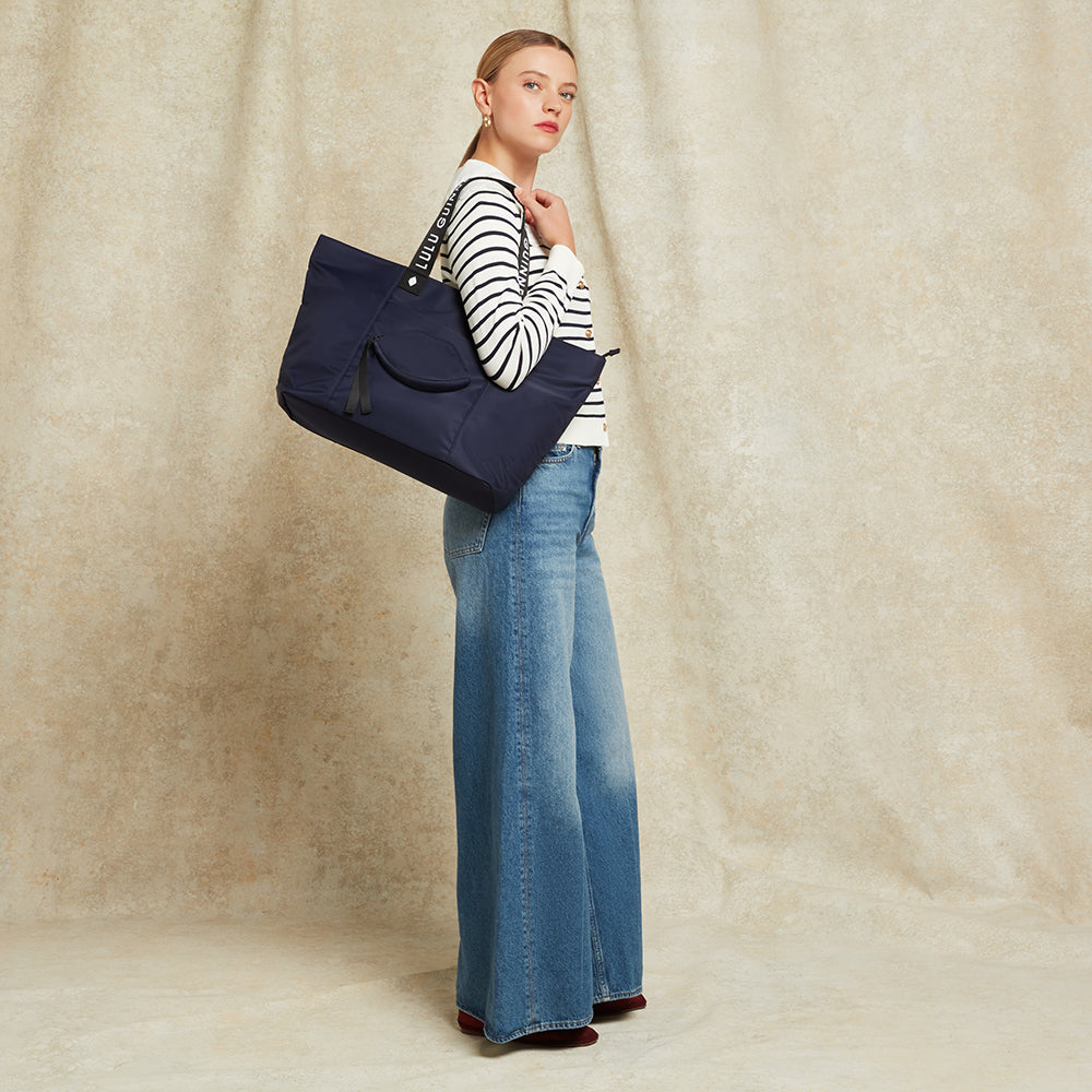 Woman holding a navy blue tote bag against a beige curtain background