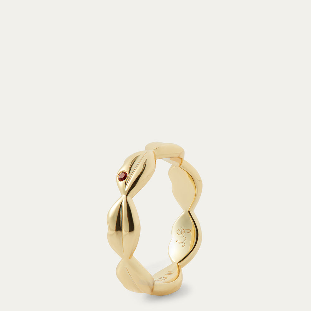 Gold ring with a small red gemstone on a light grey background