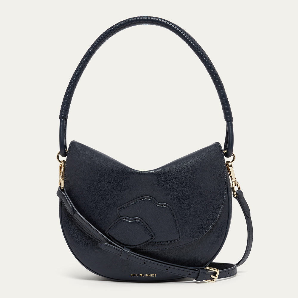 Navy leather handbag with a corded handle, crossbody strap with gold buckle and lip details on a light grey background