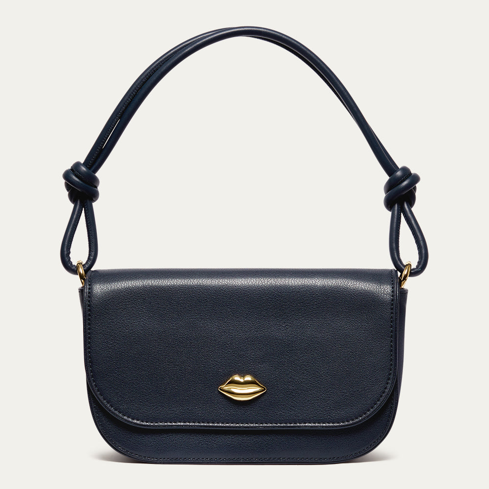 Navy blue leather shoulder bag with a gold lip on the front and a knotted shoulder strap on a light grey background