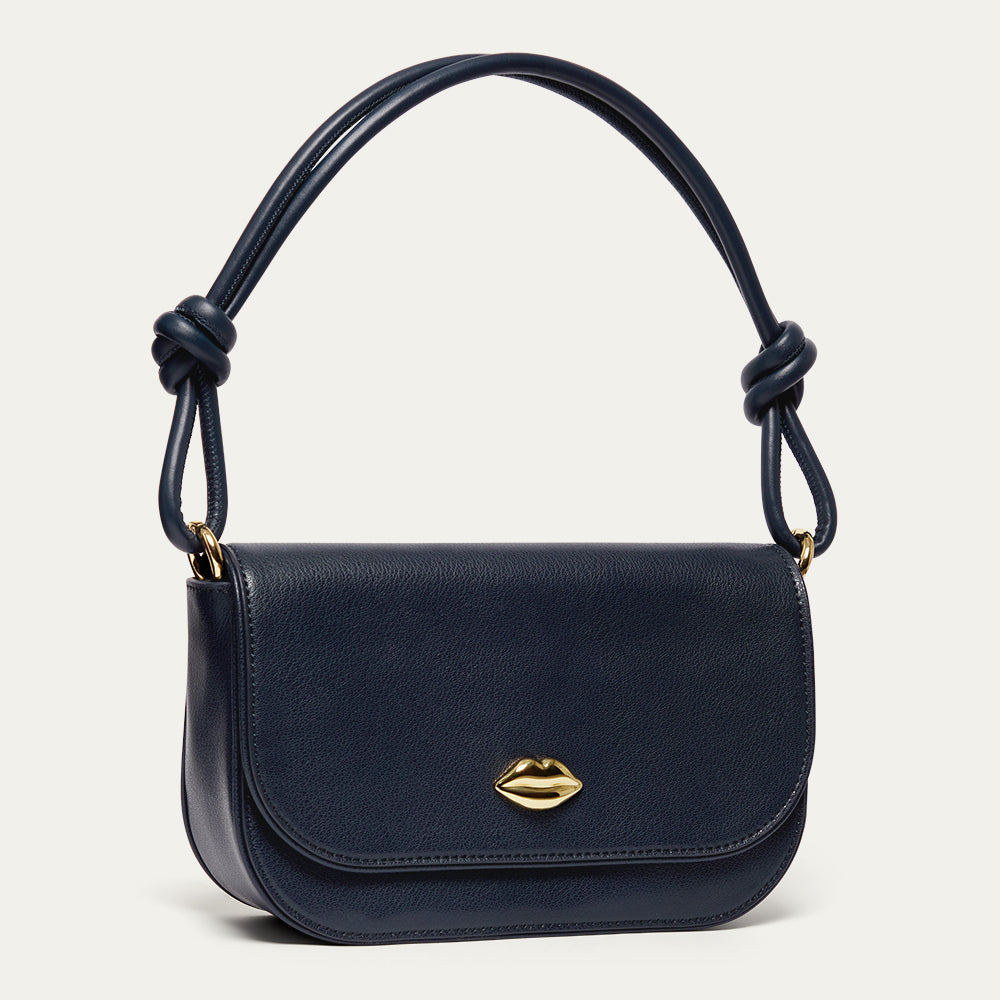 Navy blue leather shoulder bag with a gold lip on the front and a knotted shoulder strap on a light grey background