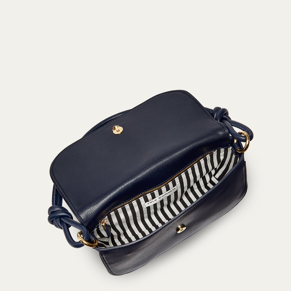 Navy blue leather shoulder bag with gold accents open revealing a black and white striped lining on a light grey background