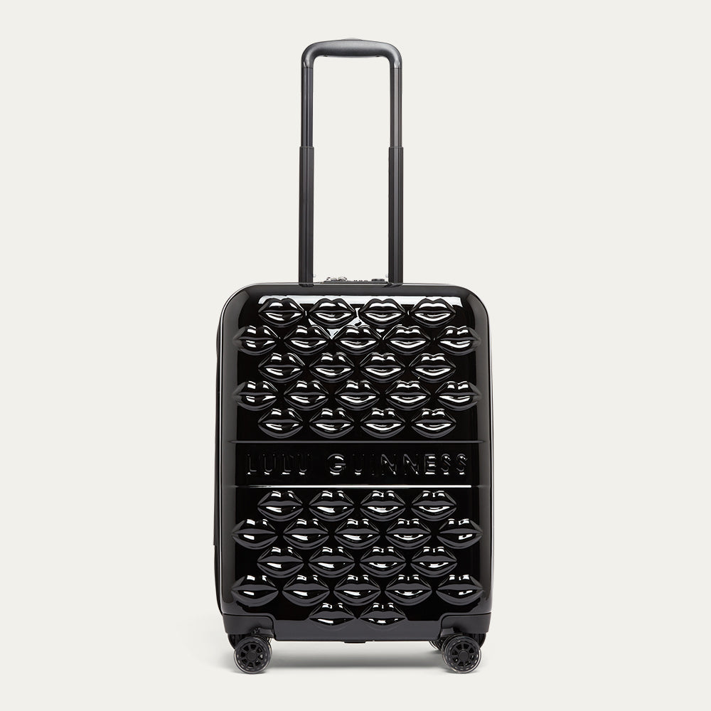 Black suitcase with top handle up, lip pattern and 'Lulu Guinness' branding on a white background