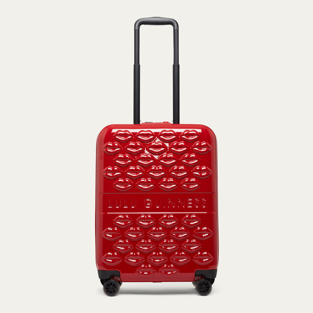 Red suitcase with top handle up, lip pattern and 'Lulu Guinness' branding on a white background