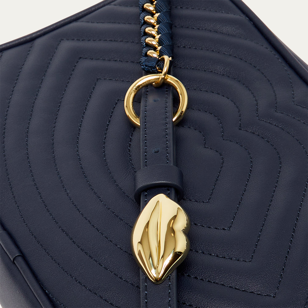 Navy blue quilted leather handbag with gold lip accents on a light grey background