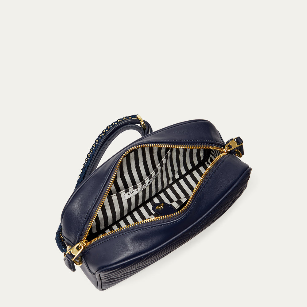 Inside image of a navy blue leather handbag with gold zipper revealing a black and white striped lining and inside pocket on a light grey background