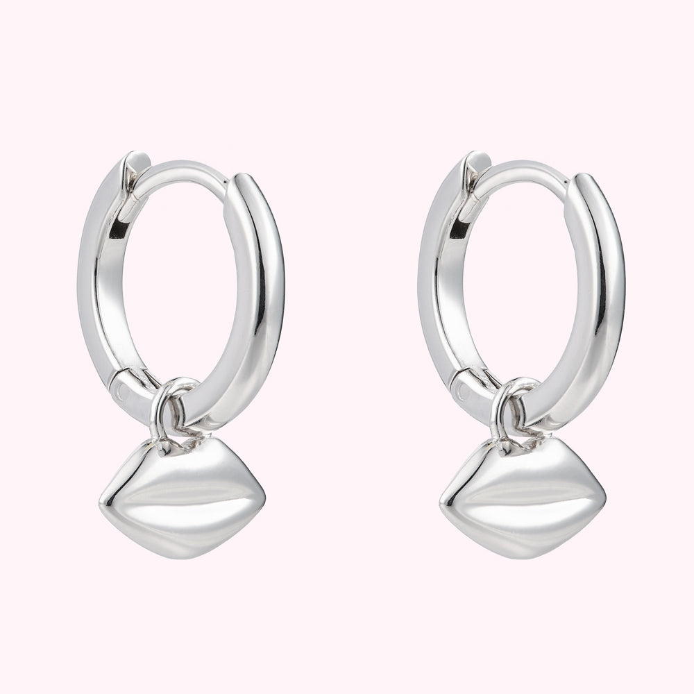Angled image of a pair or sterling silver hoop earrings with lip charms.