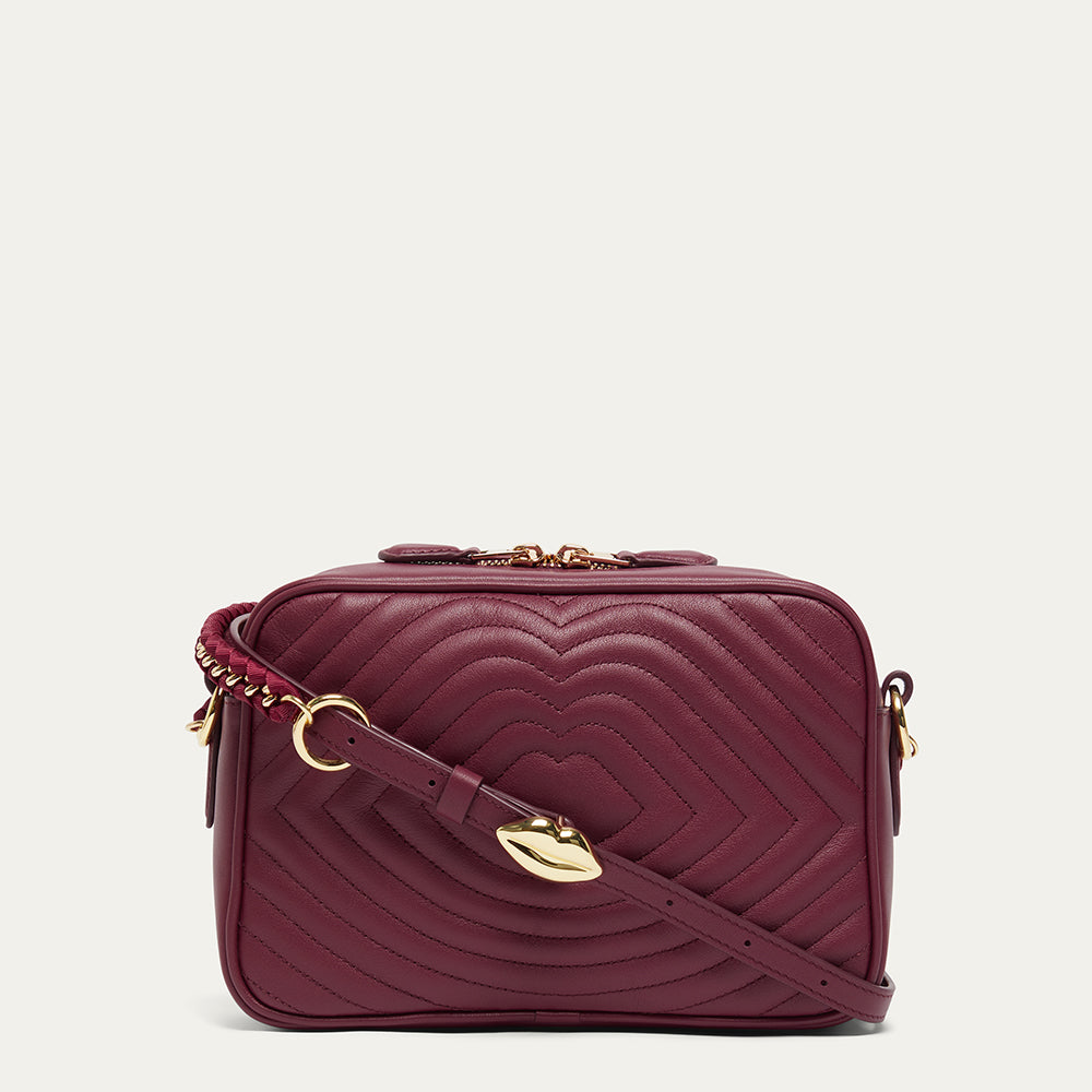 Burgundy leather quilted  crossbody handbag with gold accents on a light grey background