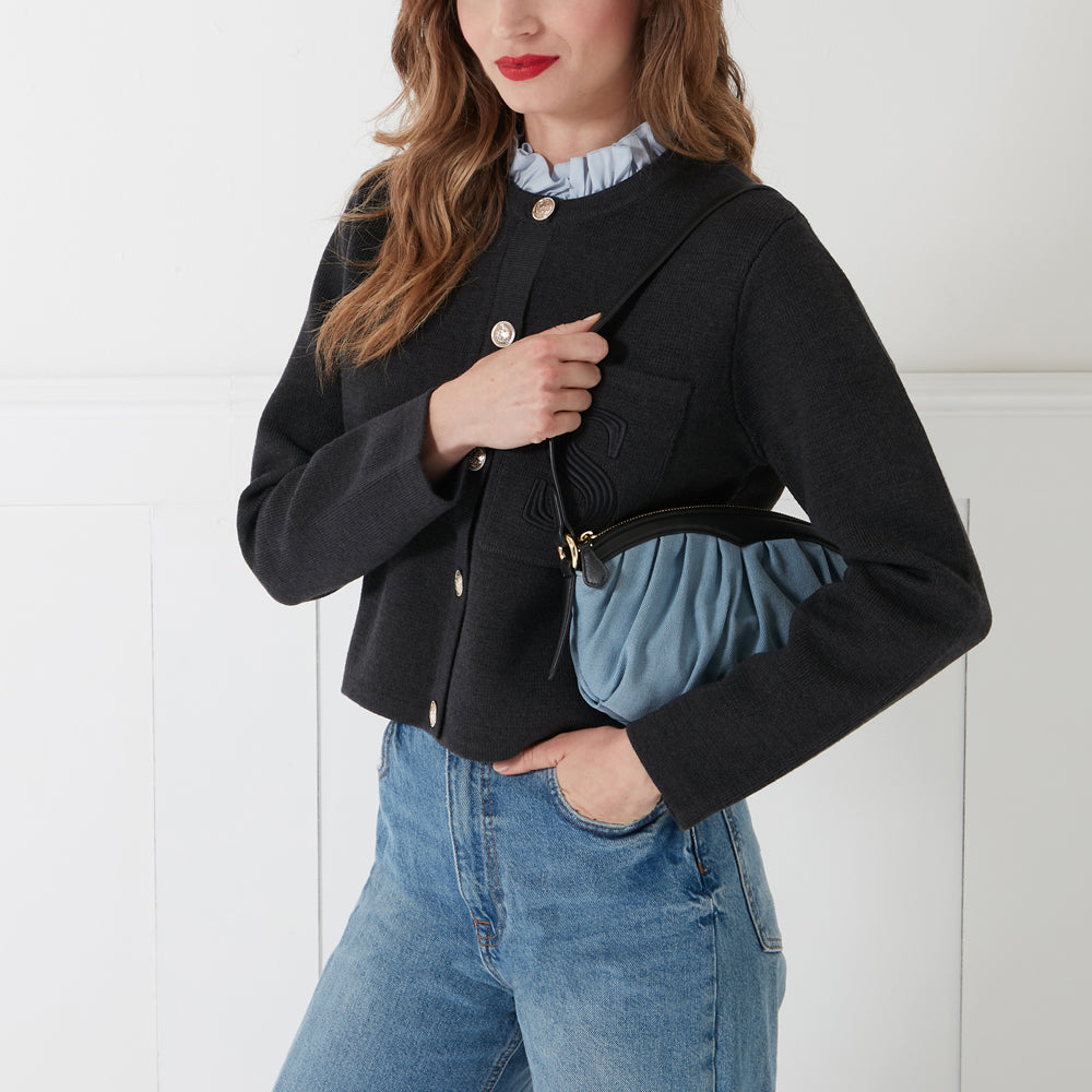 Woman in black cardigan holding light blue denim handbag against white background.
