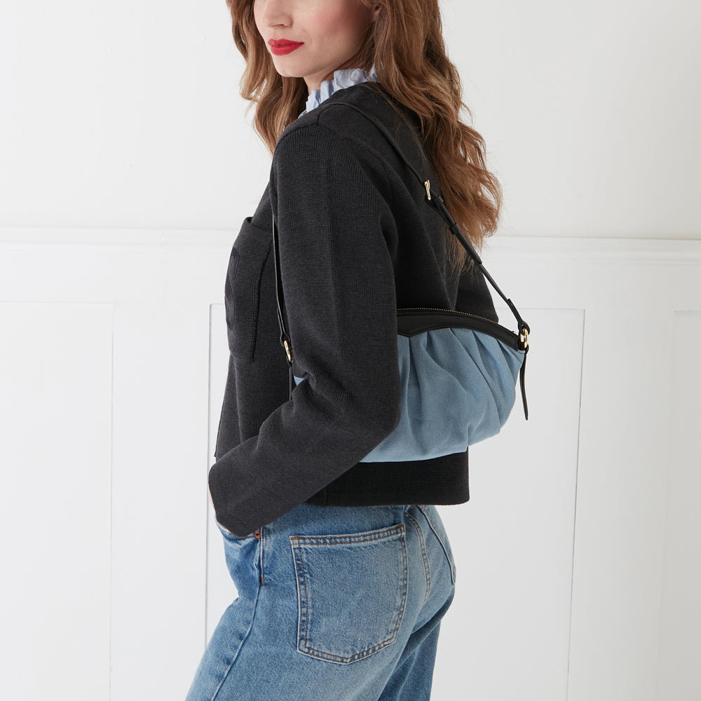 Woman wearing a dark grey sweater and blue jeans with a light blue and black shoulder bag.