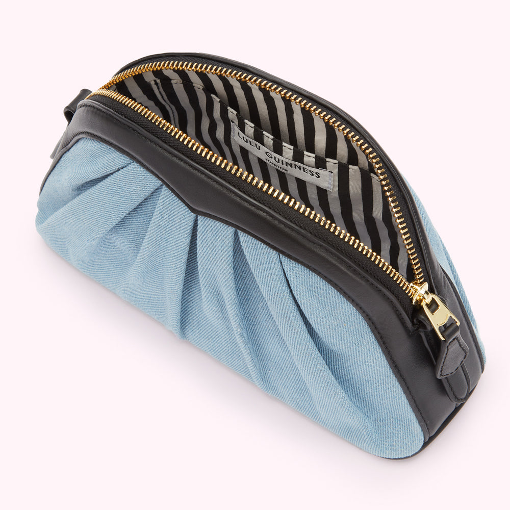 Light blue denim Lulu Guinness makeup bag with black leather trim, gold zipper, and black and white striped interior lining.
