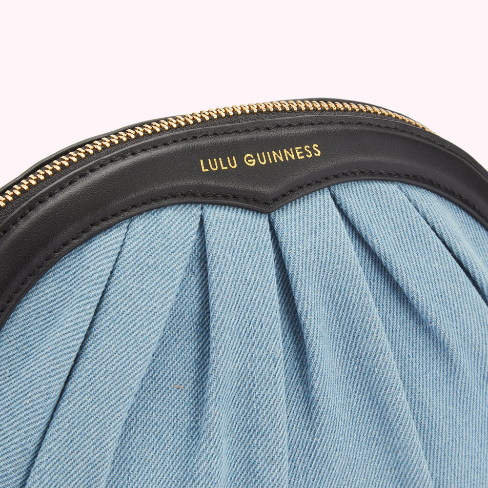 Close-up of a Lulu Guinness pleated denim purse with a black leather trim and gold zipper.
