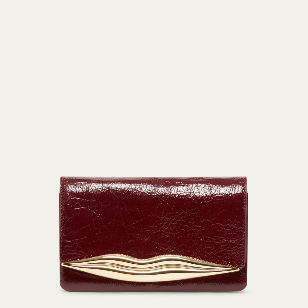 A burgundy textured leather clutch bag with a gold-tone metal lip-shaped accent across the front, shown against a light off-white background.