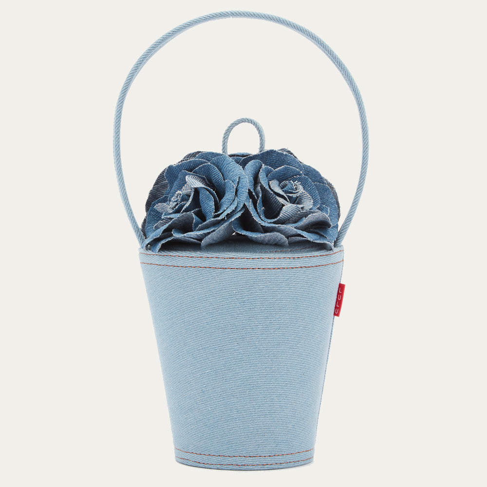 Light blue denim handbag shaped like a bucket with two denim roses on top and a top handle.