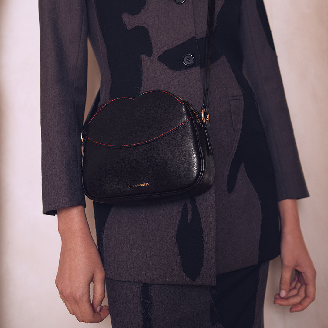 Person wearing a dark coat with a black handbag on a plain background