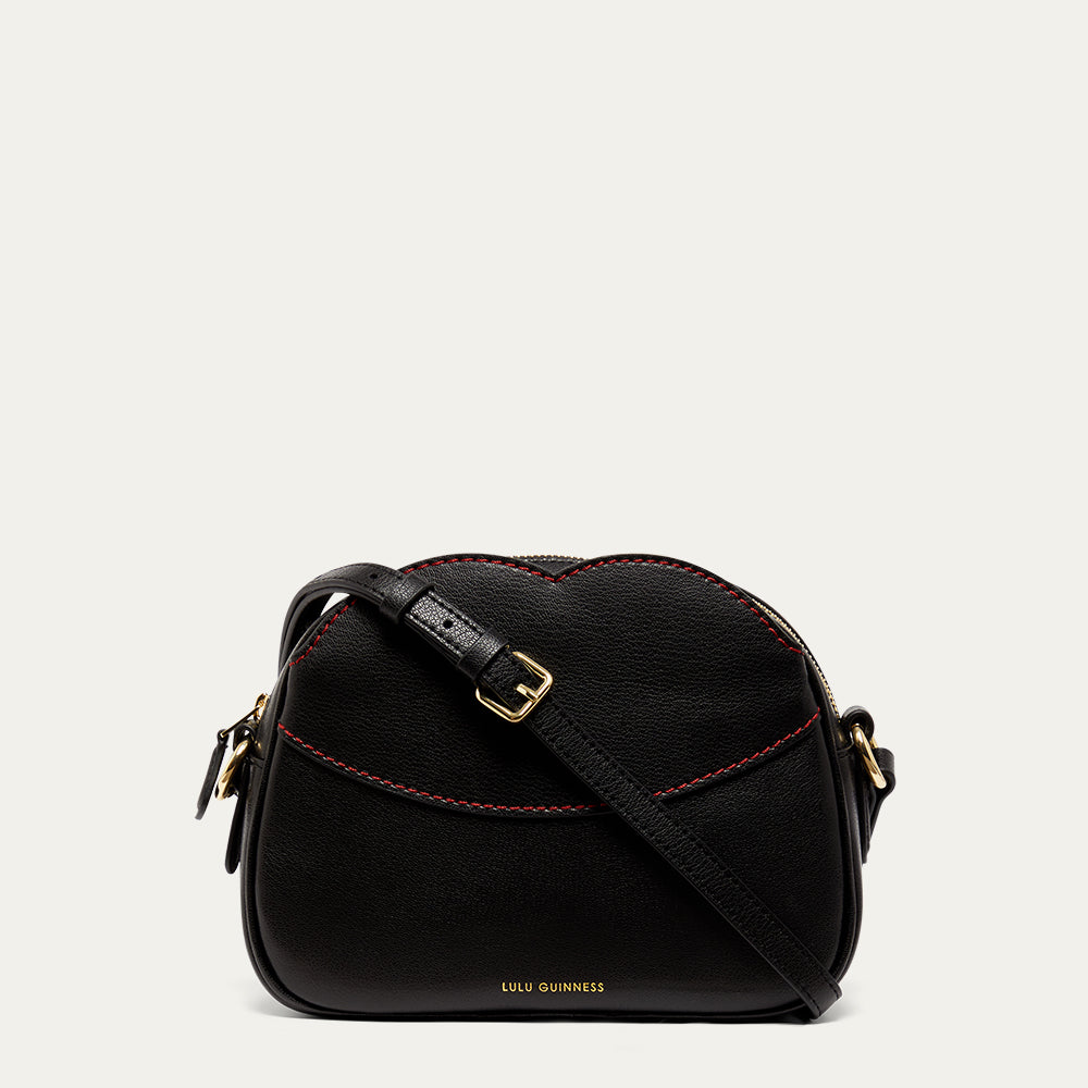 Black leather crossbody handbag with red stitching and gold accents on a light beige background