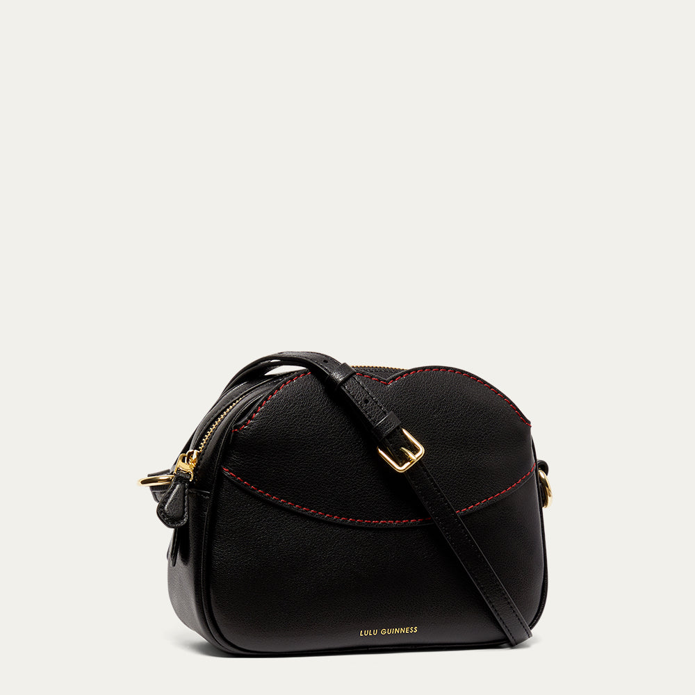 Black leather crossbody handbag with red stitching and gold accents on a light grey background