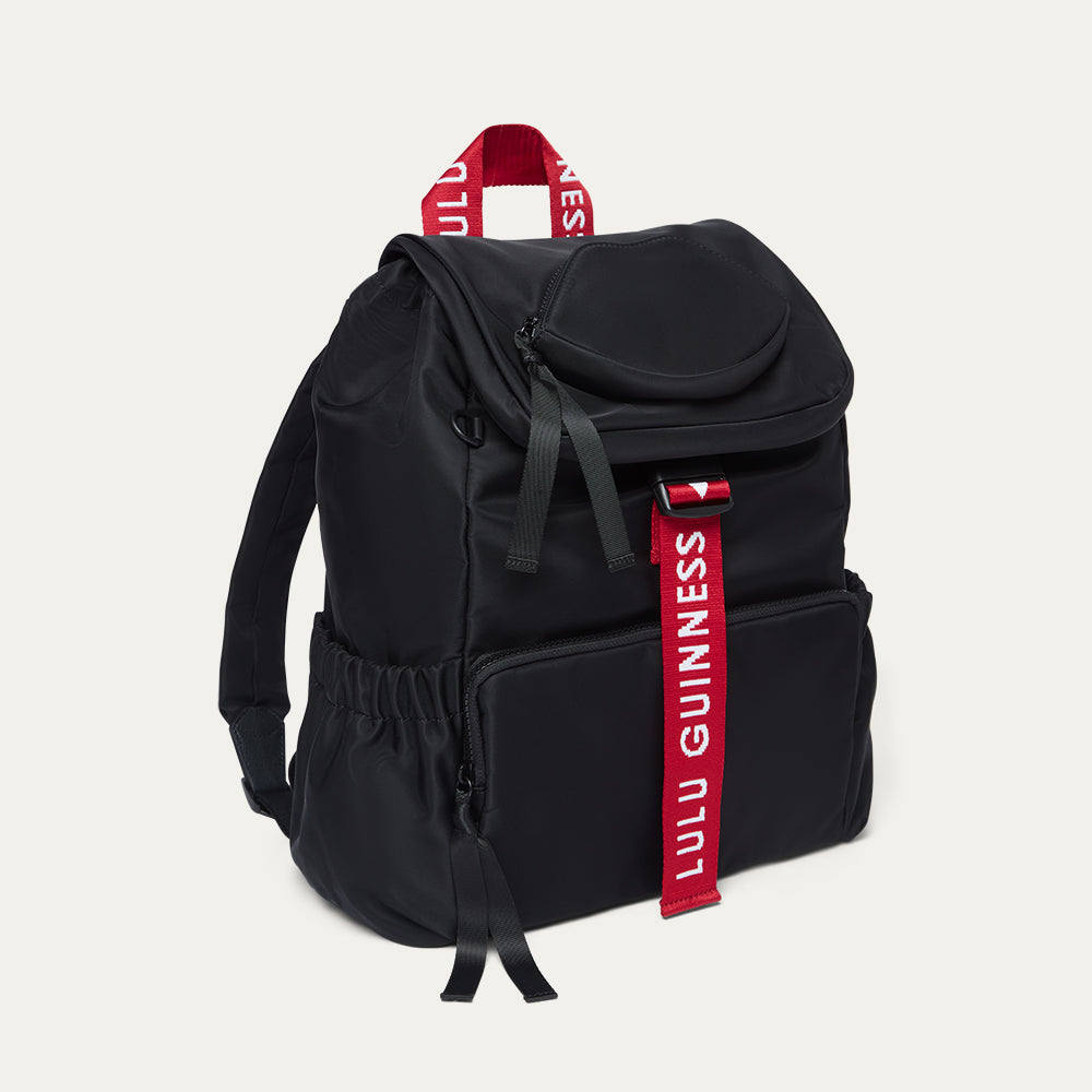Black backpack with red Lulu Guinness strap on a light grey background