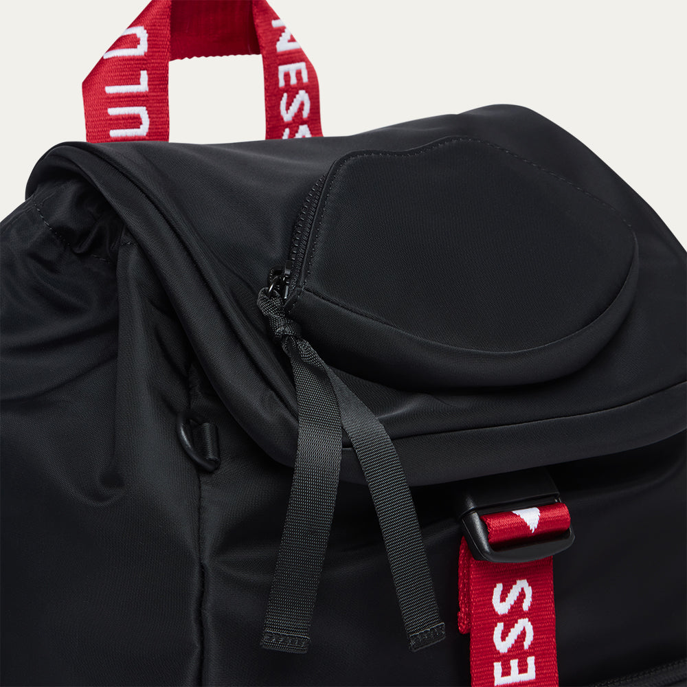 Black backpack with red and white 'Lulu Guinness' straps on a light grey background