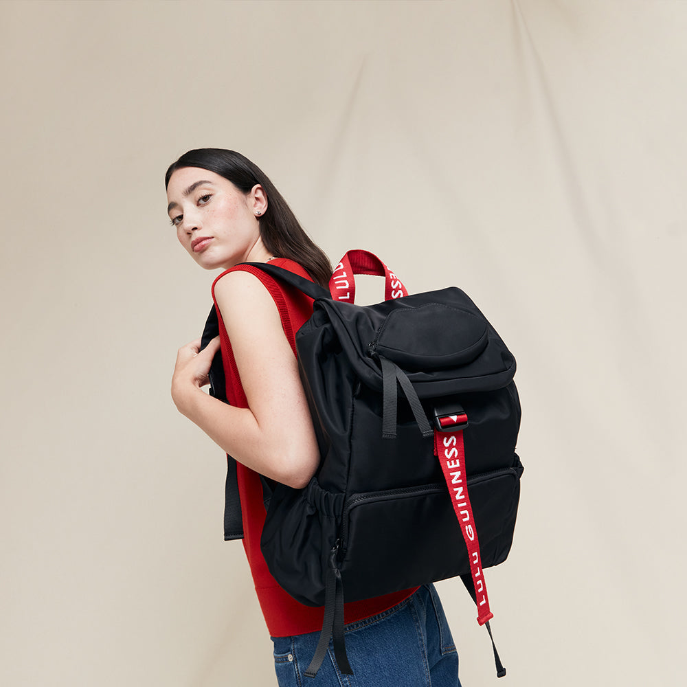 Person wearing a black backpack with red straps on a beige background
