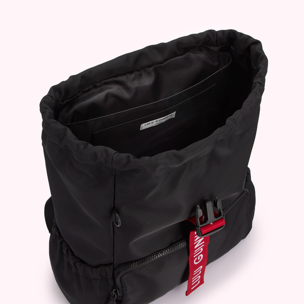 Black Lulu Guinness backpack with red logo detail, viewed from above, showing the inside of the bag.
