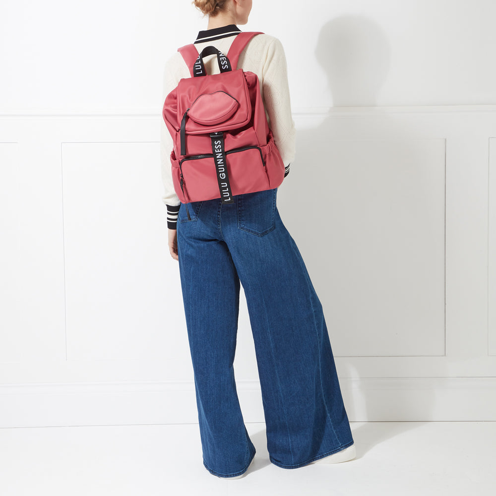 A woman from behind wearing wide-leg jeans and a blush pink Lulu Guinness backpack with a lip-shaped pocket.