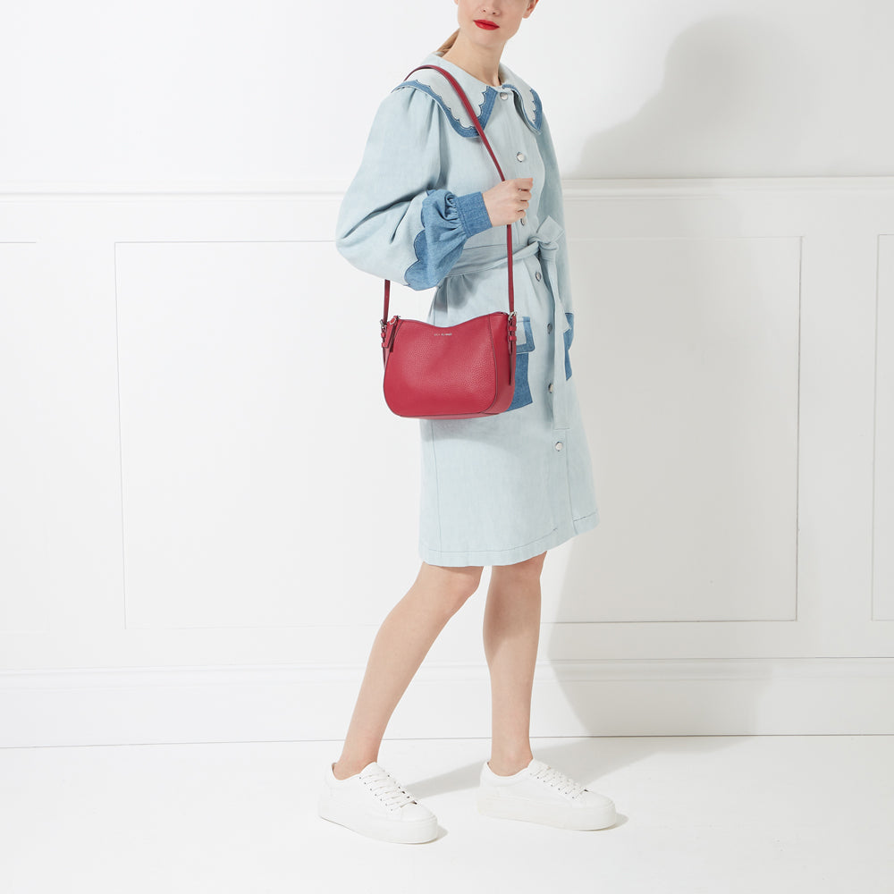 Woman in light blue dress carrying a red crossbody bag against a white background.