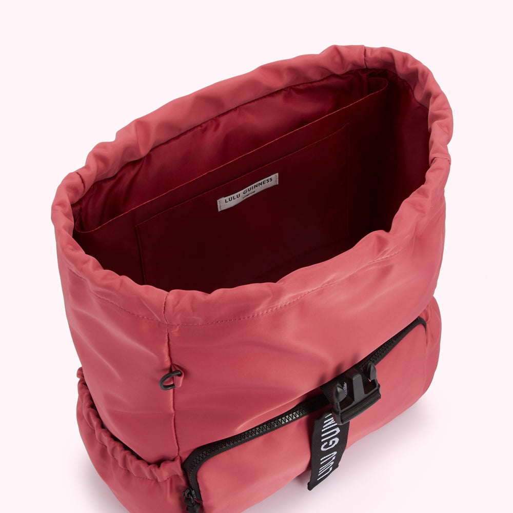 Inside of a dusty rose Lulu Guinness backpack with black zipper details and a small interior pocket.