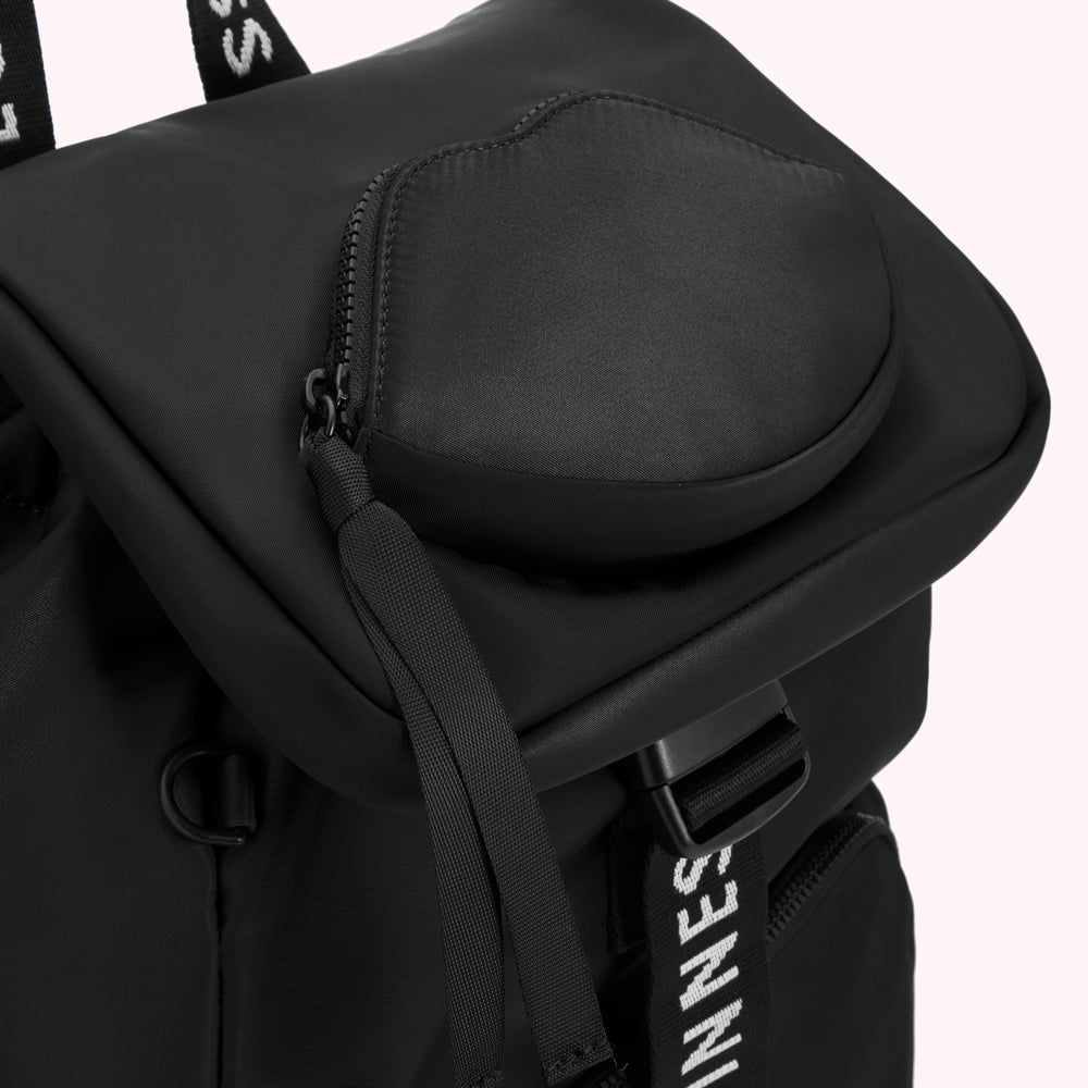 Close-up of a black backpack with a heart-shaped pocket and branded straps.
