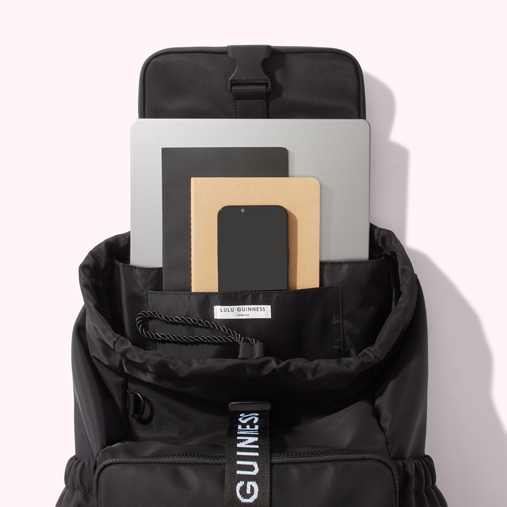 Open black Lulu Guinness backpack with laptop, notebooks and phone inside.