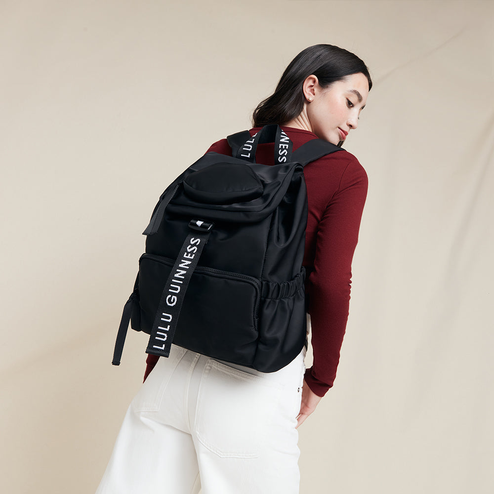 Person wearing a black backpack with 'Lulu Guinness' branding on a beige background
