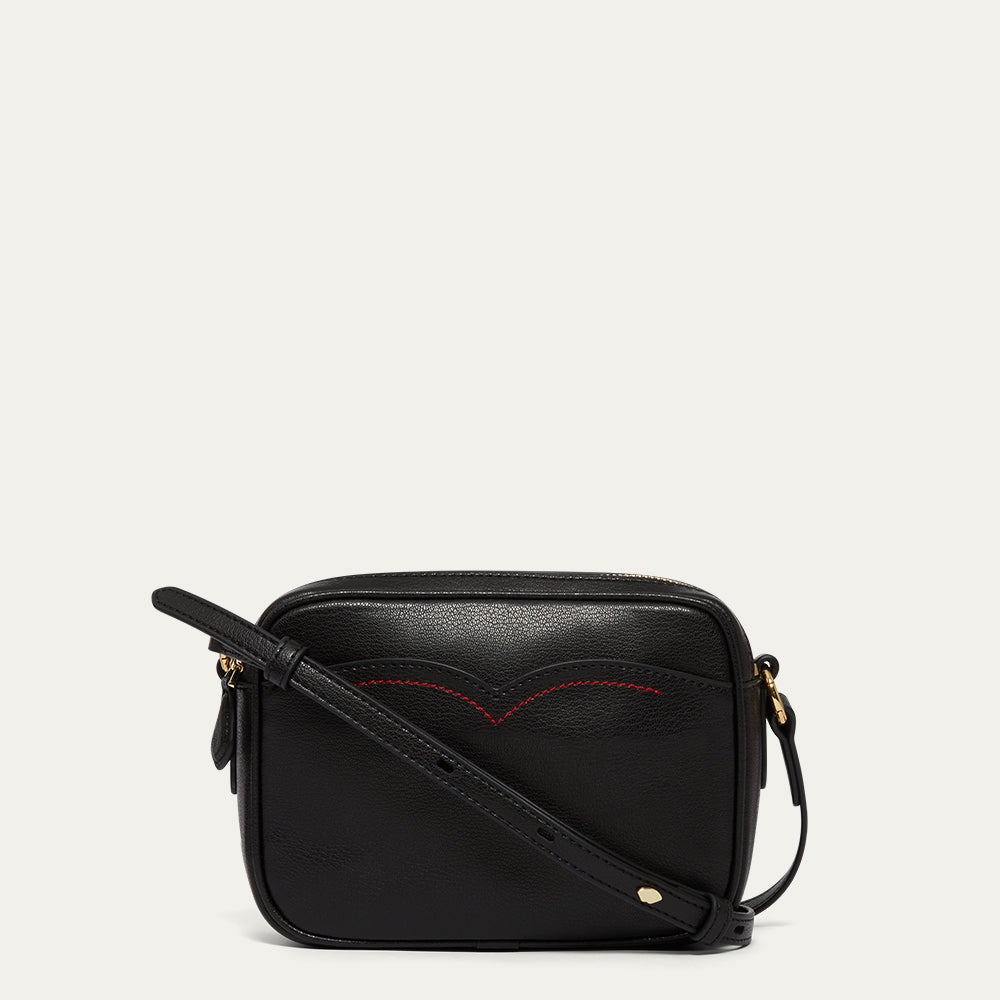 Black leather crossbody bag with red stitching on a light grey background