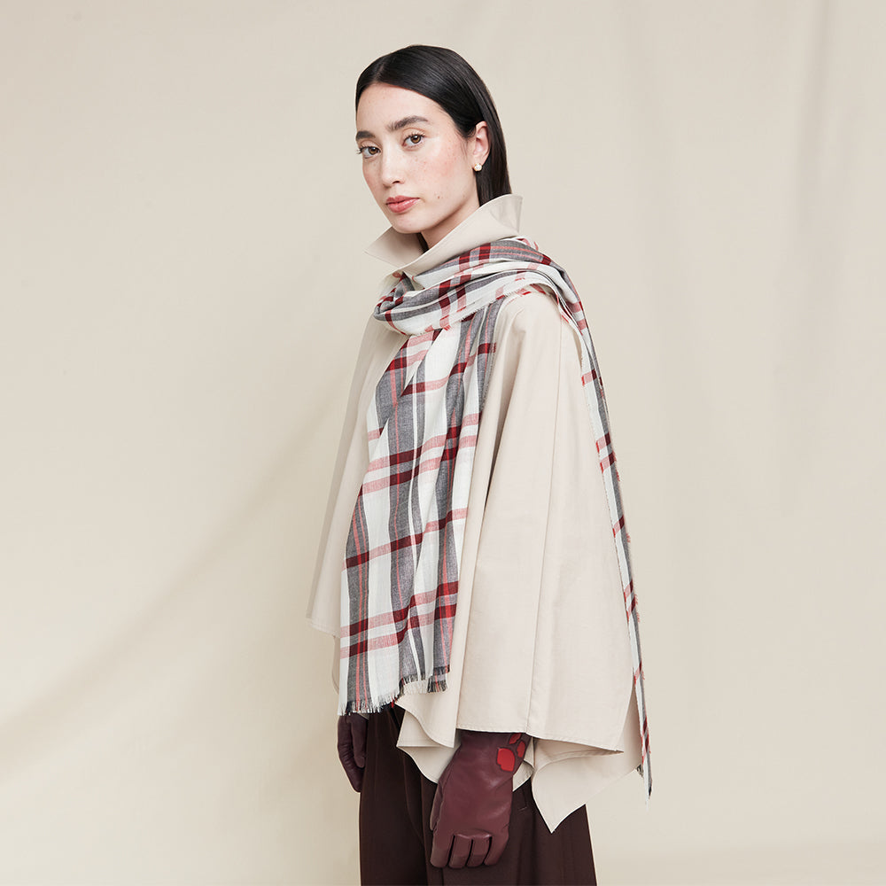 Woman wearing a plaid scarf and beige coat against a plain background