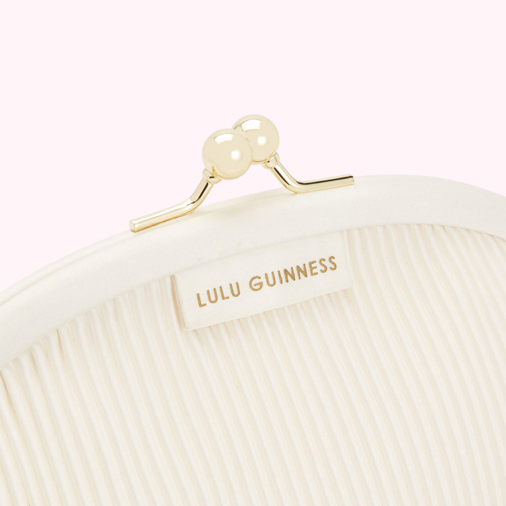 Close-up of a white Lulu Guinness purse with a gold clasp featuring two pearl-like embellishments.
