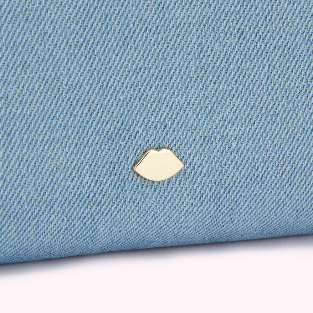 Close-up of light blue denim texture with a gold lip-shaped emblem.
